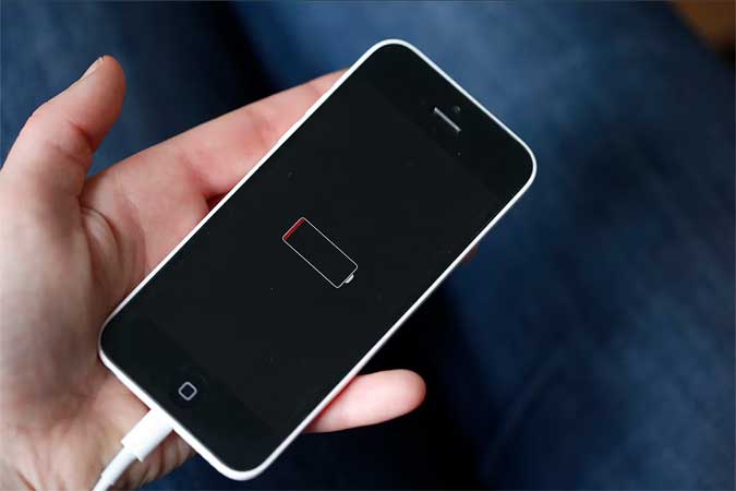 Image of a person holding their iPhone plugged in to charge with the battery drain notification displayed on the phone.