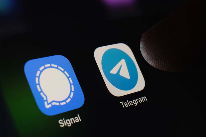 Photo of thumb hovering over Signal and Telegram apps on a smartphone.